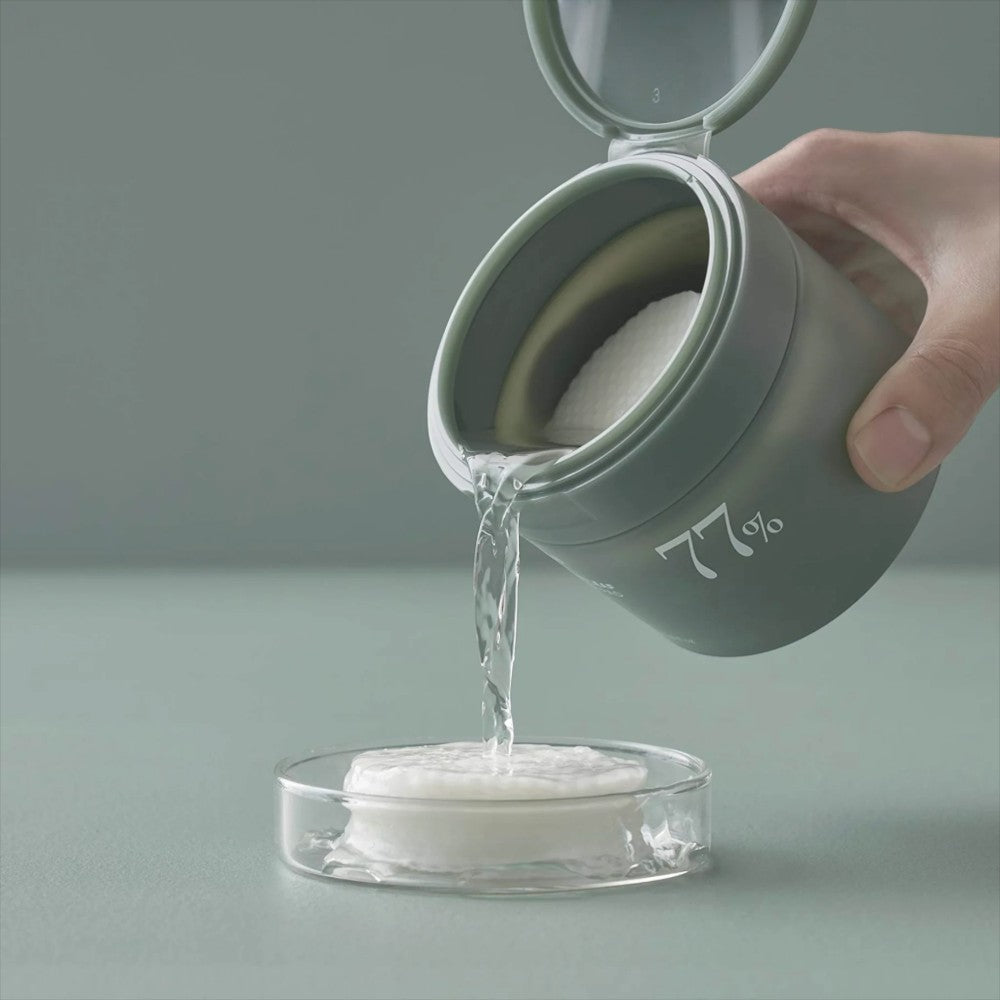 Skin TOGO ANUA Heartleaf 77% Clear Pad toner pads being poured from a green container into a glass dish
