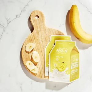 Skin TOGO A'pieu Milk One Pack banana sheet masks on a wooden cutting board with fresh banana slices