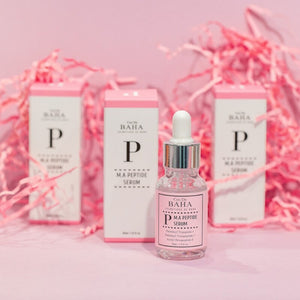 Skin TOGO Cos De BAHA P.M.A Peptide Serum bottle and boxes on a pink background with decorative paper shreds.