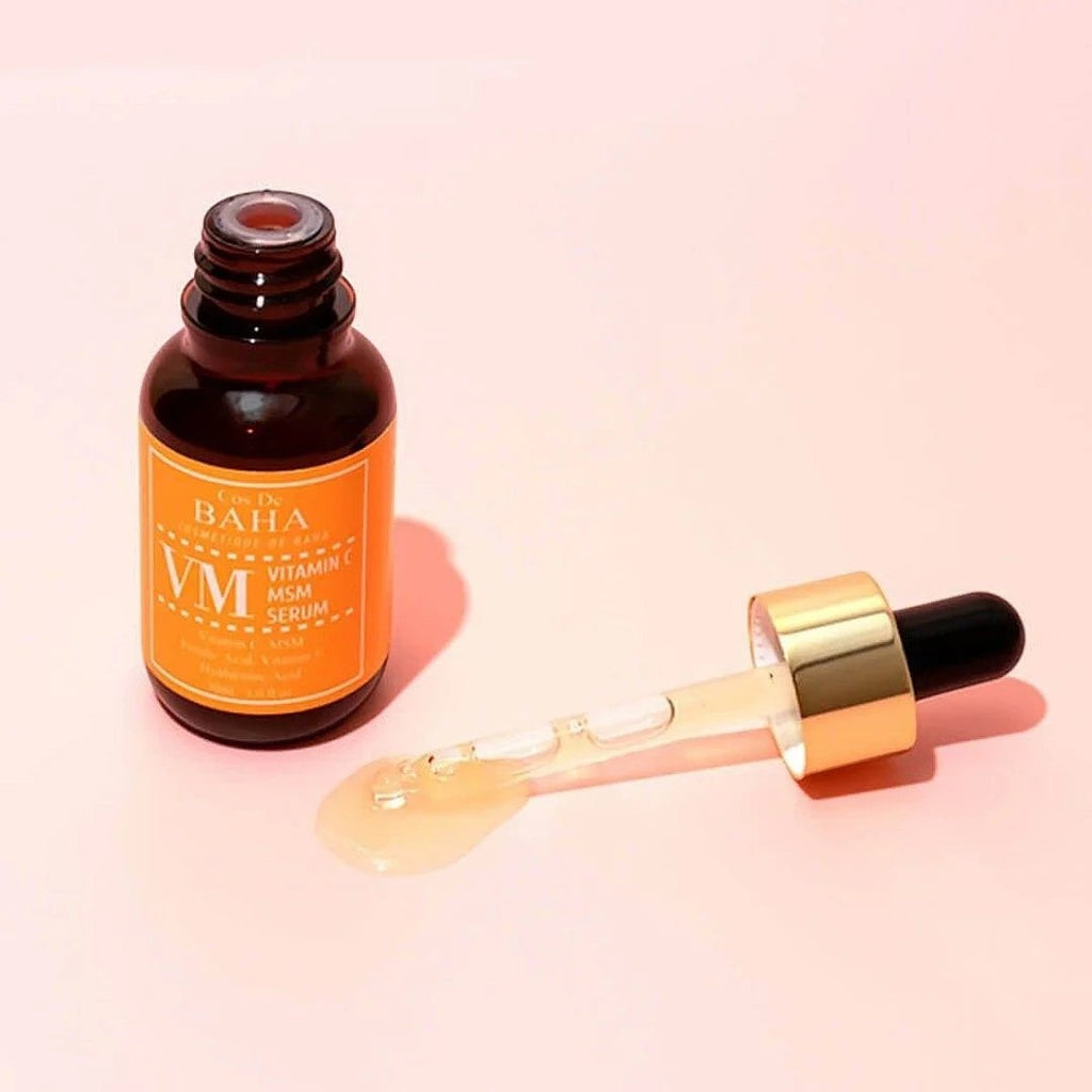 Skin TOGO Cos De BAHA VM Vitamin C MSM serum in a brown glass bottle with a gold dropper on a soft pink background.