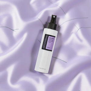 Skin TOGO COSRX AHA/BHA Clarifying Treatment Toner in a white spray bottle on a soft, draped lavender fabric background.