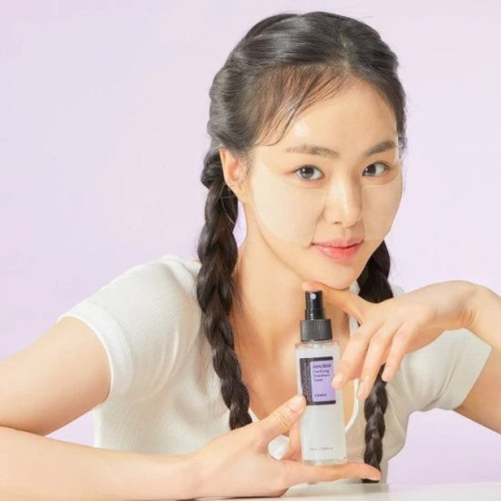 Skin TOGO model holding a COSRX AHA/BHA Clarifying Treatment Toner spray bottle with under-eye patches applied