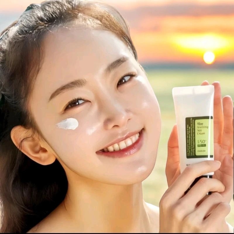 Skin TOGO model smiling with Cosrx Aloe Soothing Sun Cream SPF50 on her cheek against a sunset beach background.