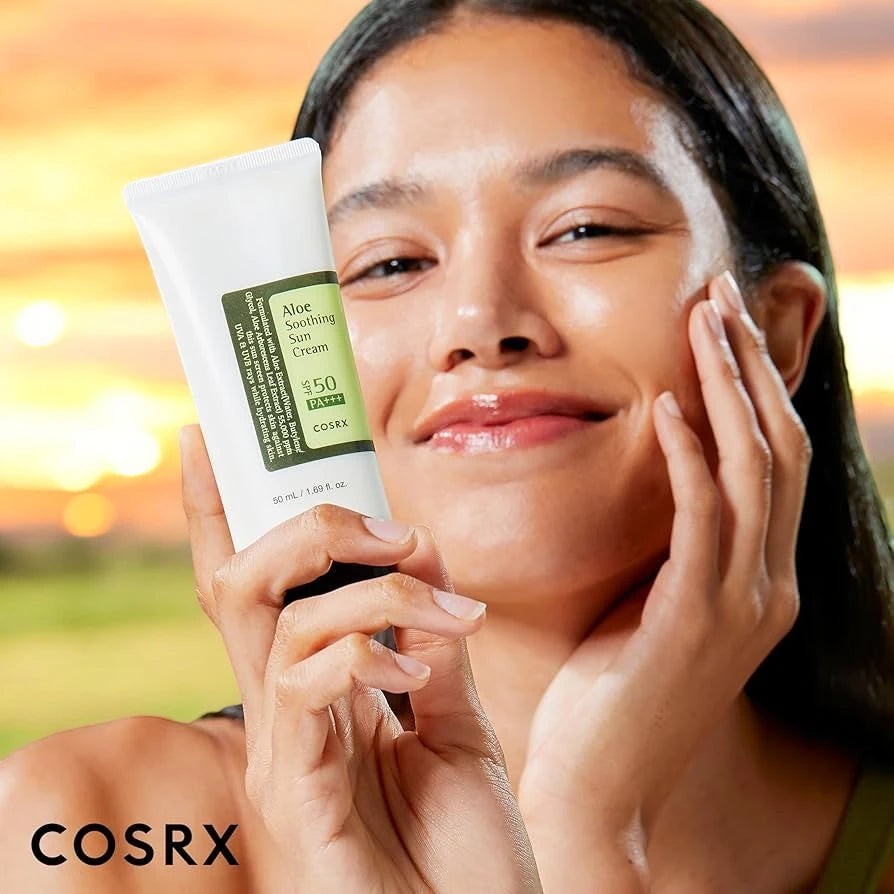 Skin TOGO model holding Cosrx Aloe Soothing Sun Cream SPF50 PA+++ tube against a sunset background