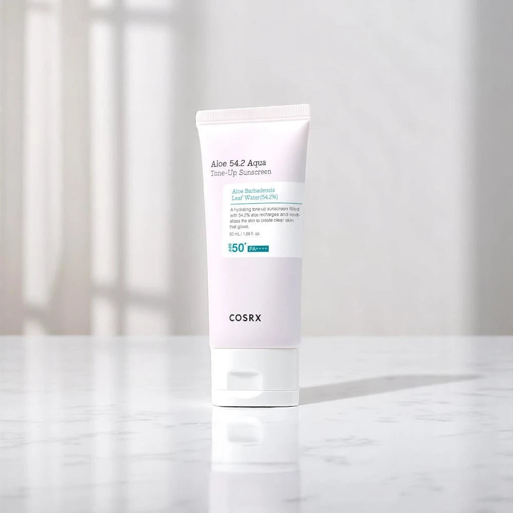 Skin TOGO COSRX Aloe 54.2 Aqua Tone-Up Sunscreen SPF50+ in a white tube on a marble surface with soft lighting.