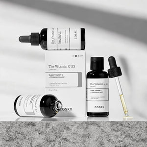 Skin TOGO Cosrx The Vitamin C 23 serum bottles and box with dropper on a stone surface for brightening skincare