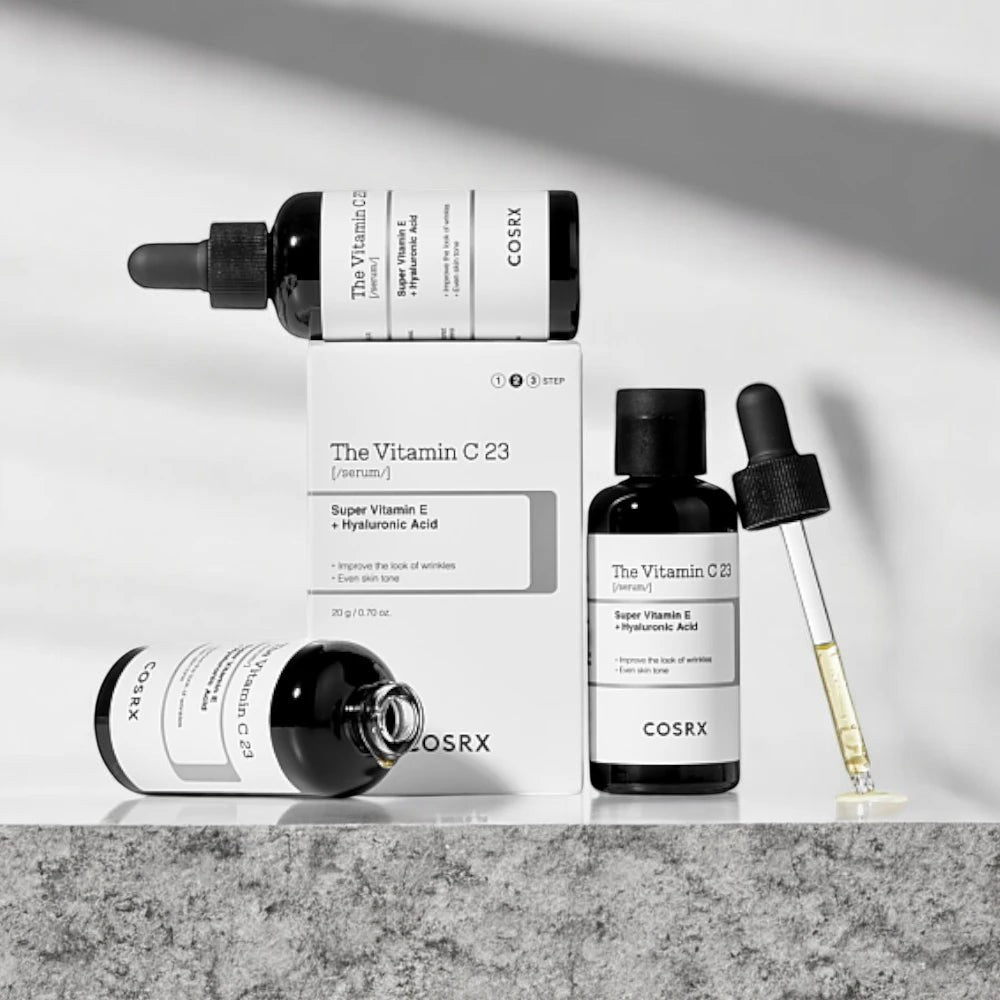Skin TOGO Cosrx The Vitamin C 23 serum bottles and box with dropper on a stone surface for brightening skincare