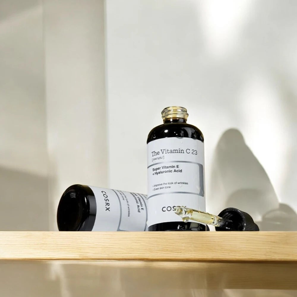 Skin TOGO Cosrx The Vitamin C 23 Serum bottles with dropper on a wooden shelf for brightening and anti-aging care.