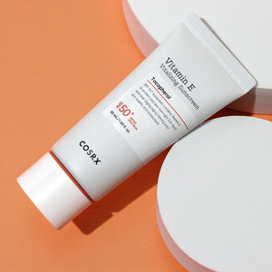Skin TOGO COSRX Vitamin E Vitalizing Sunscreen SPF 50+ in a white 50ml tube on a minimalist orange and white display.