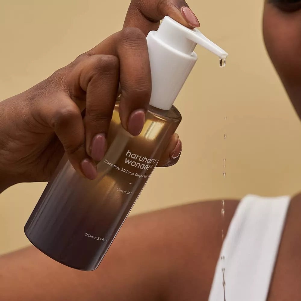 Skin TOGO Haruharu WONDER Black Rice Deep Cleansing Oil in a pump bottle being applied by a person with dark skin.
