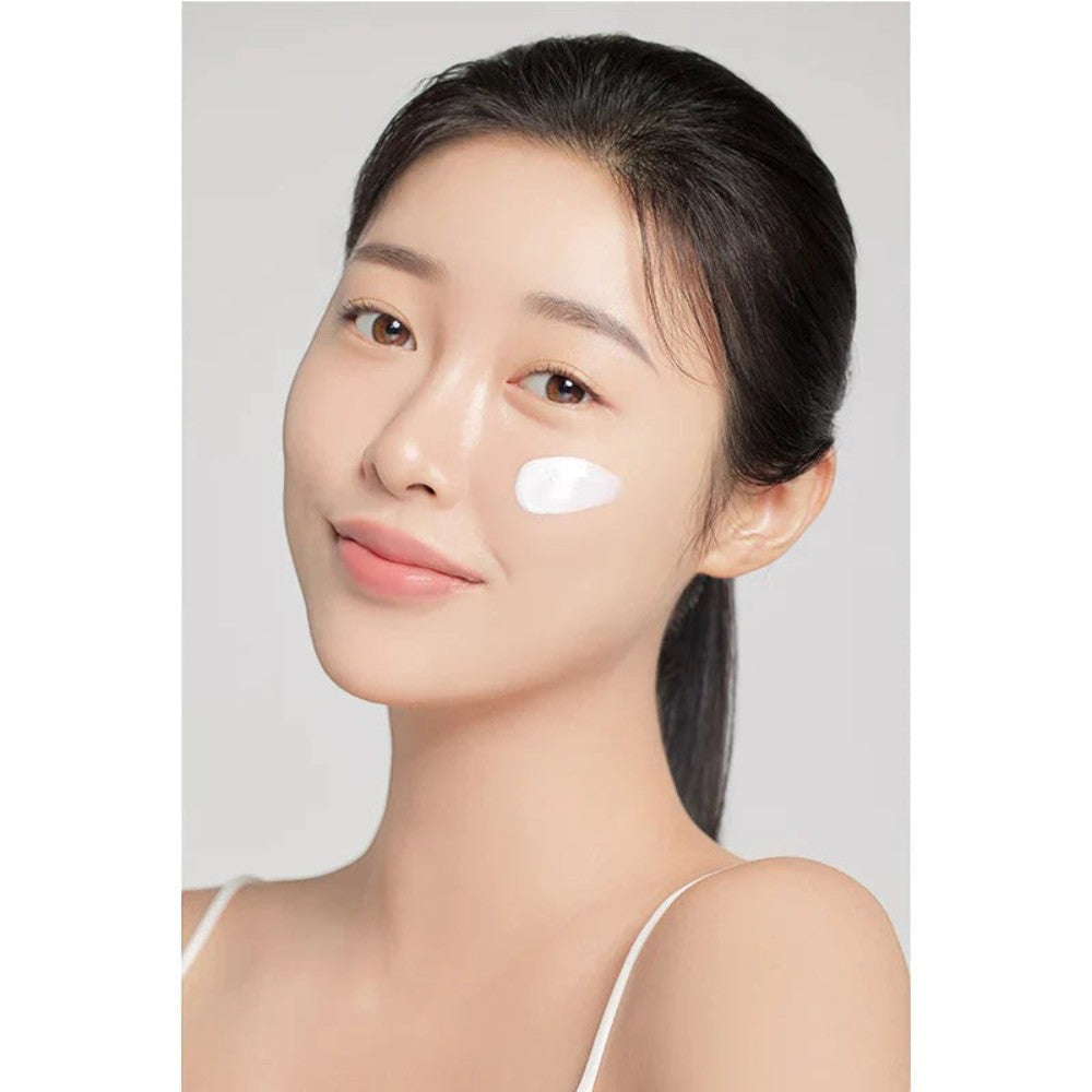 Skin TOGO model applying I'm from Rice Sunscreen SPF50+ with a creamy white texture on her cheek for radiant skin.