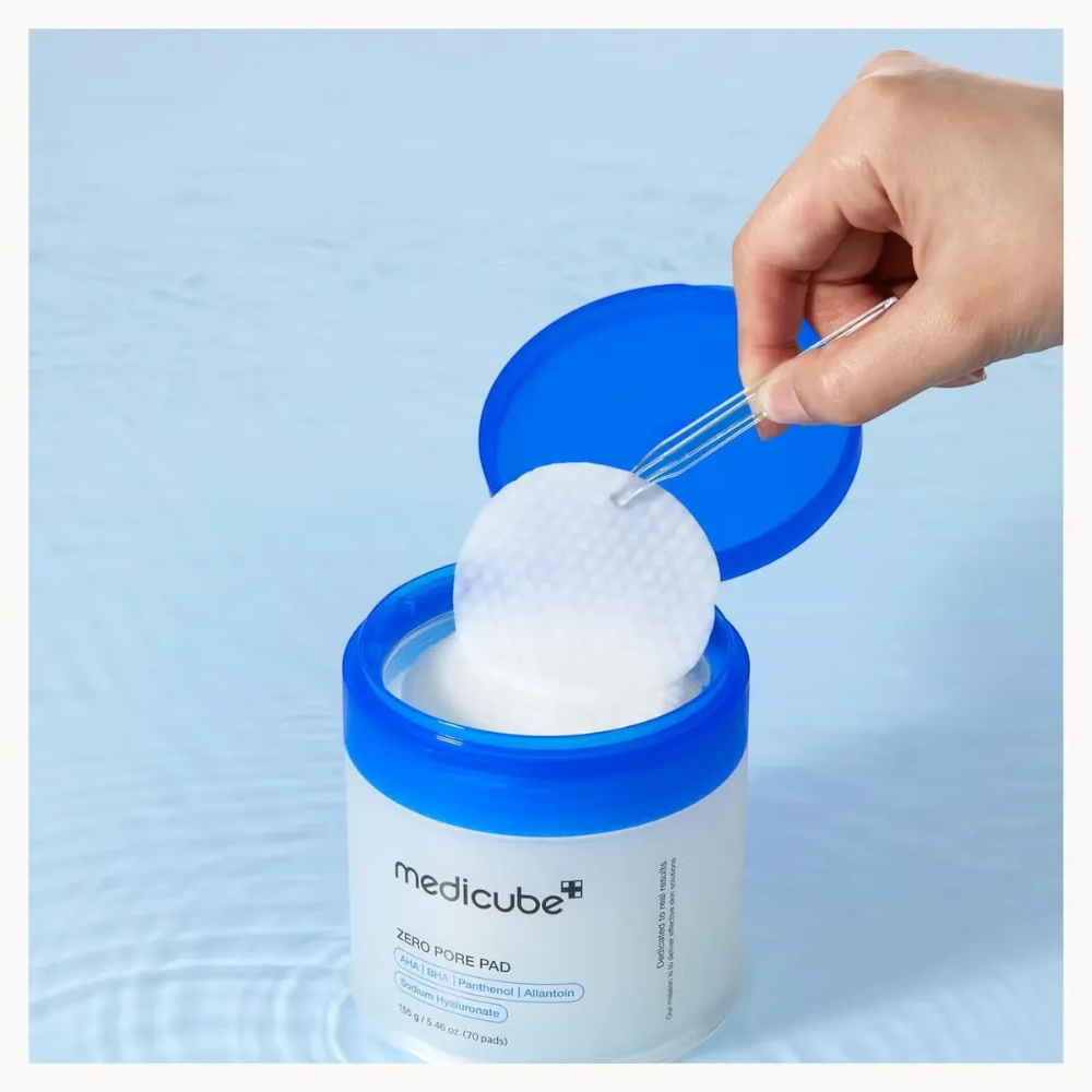 Skin TOGO Medicube Zero Pore Pad jar with blue lid, showing a hand using tweezers to lift a textured exfoliating pad.