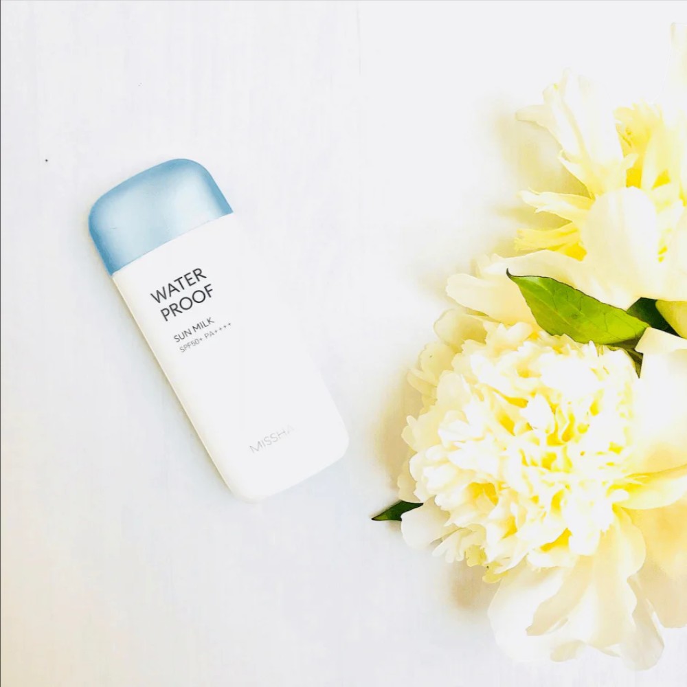 Skin TOGO MISSHA All Around Safe Block Waterproof Sun Milk bottle with SPF50+ PA++++ next to white peony flowers.