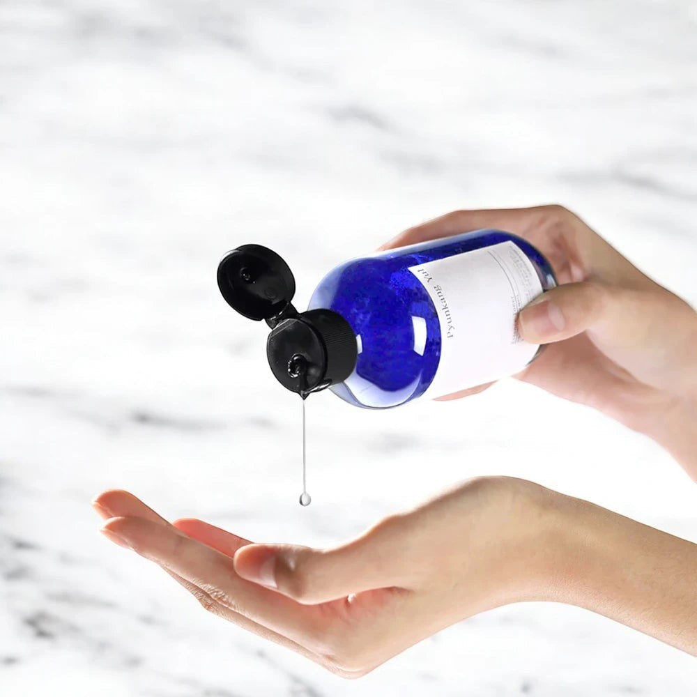 Skin TOGO Pyunkang Yul Essence Toner being poured from a blue bottle into a hand for skincare application.