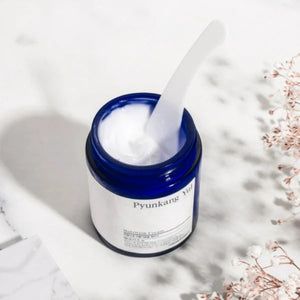 Skin TOGO Pyunkang Yul Moisture Cream in a blue glass jar with a white spatula, set on a marble surface.