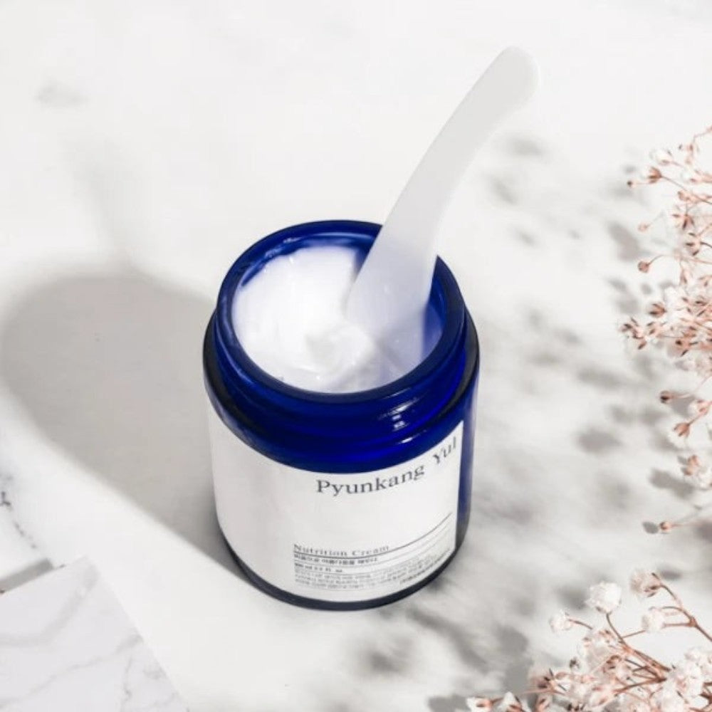 Skin TOGO Pyunkang Yul Moisture Cream in a blue glass jar with a white spatula, set on a marble surface.