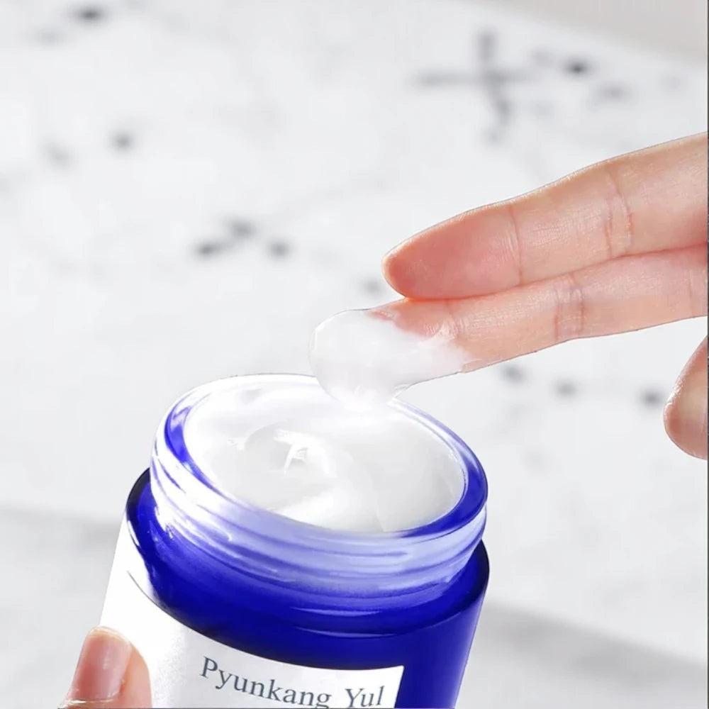 Skin TOGO Pyunkang Yul Moisture Cream with a rich white texture being applied from a blue glass jar