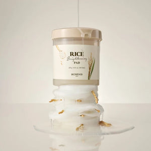 Skin TOGO SKINFOOD Rice Brightening Pad jar stacked on moist cotton pads with rice grains and essence dripping down.