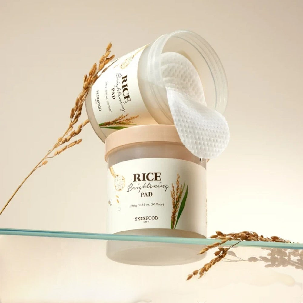 Skin TOGO SKINFOOD Rice Brightening Pads in a jar with textured cotton pads and rice stalks on a glass shelf.