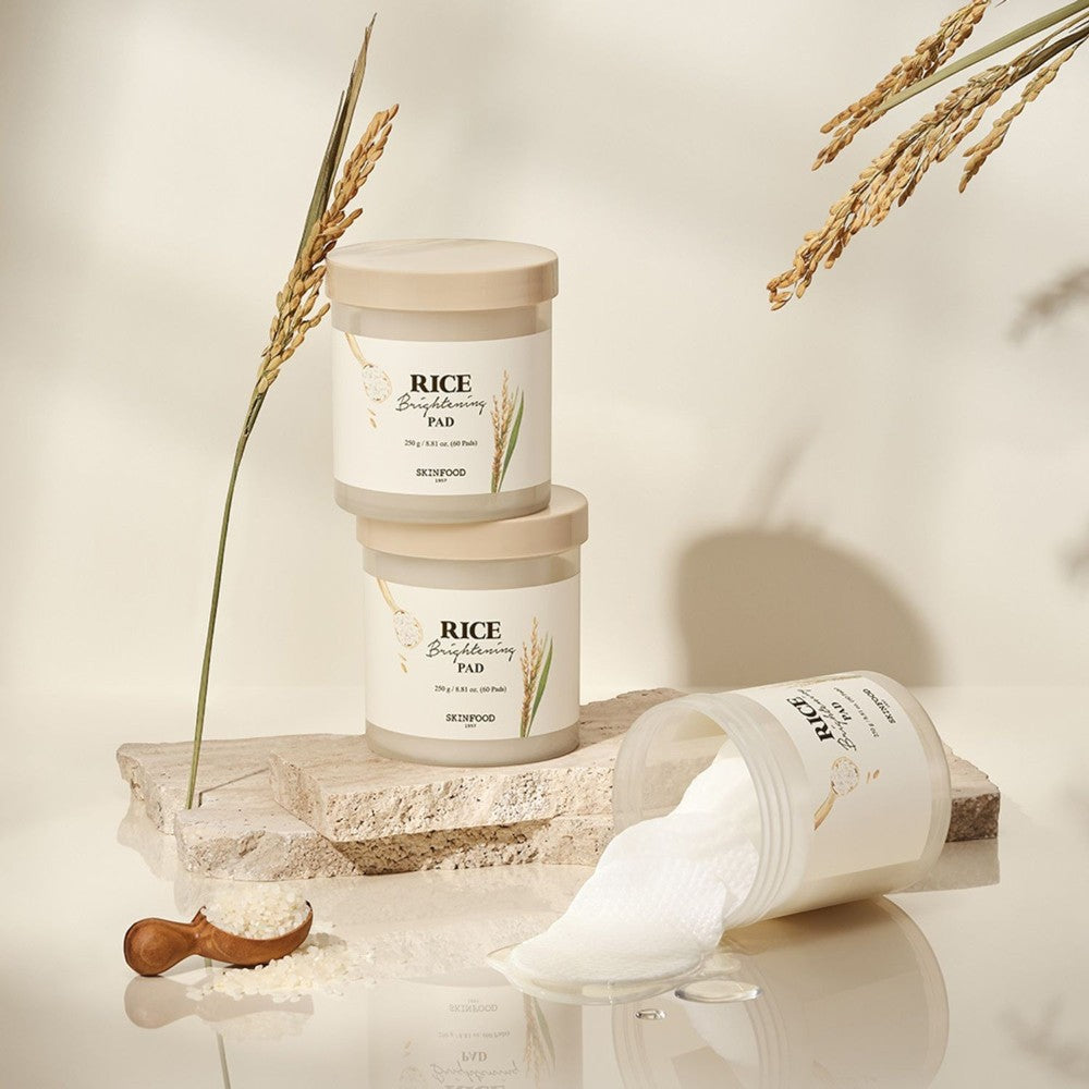 Skin TOGO SKINFOOD Rice Brightening Pads in jars with rice stalks and cotton pads on stone surfaces for skincare.