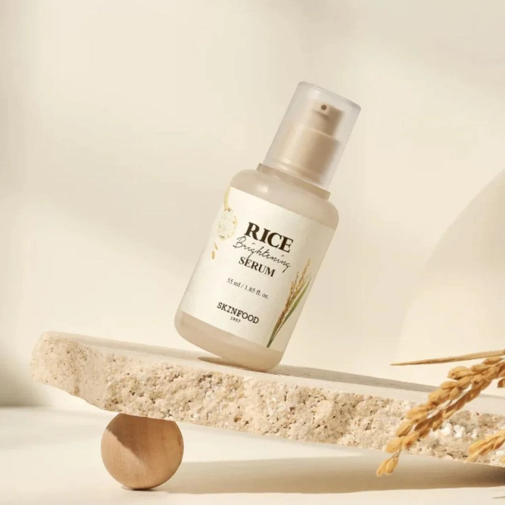 Skin TOGO SKINFOOD Rice Brightening Serum in a glass pump bottle balanced on a stone slab with dried rice stalks.