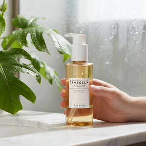 Skin TOGO SKIN1004 Madagascar Centella Light Cleansing Oil in a clear pump bottle held by a hand near a green plant.