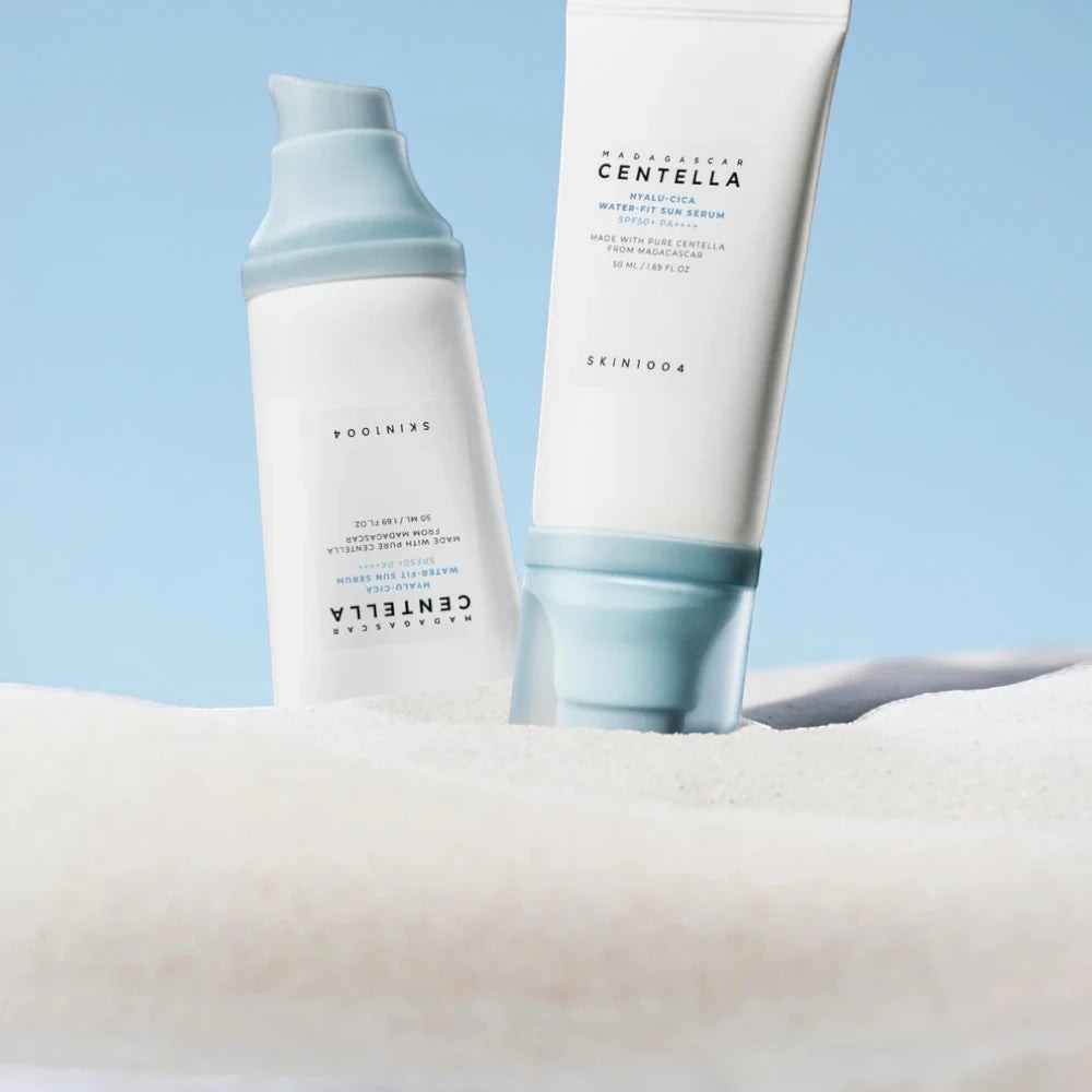 Skin TOGO SKIN1004 Madagascar Centella Hyalu-Cica Water-Fit Sun Serum bottles standing in white sand against blue sky.