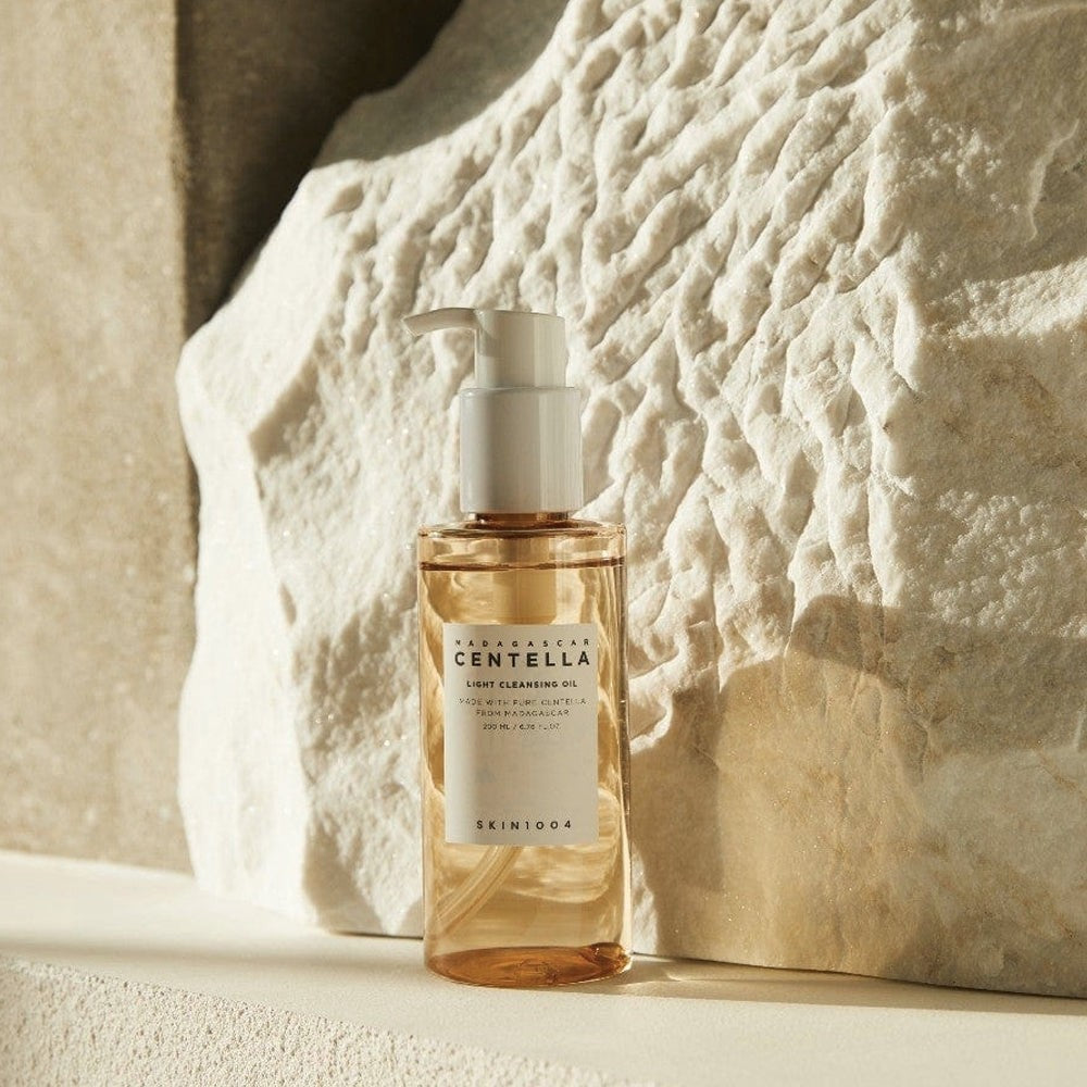 Skin TOGO SKIN1004 Madagascar Centella Light Cleansing Oil in a clear bottle with a pump, set against a textured rock.