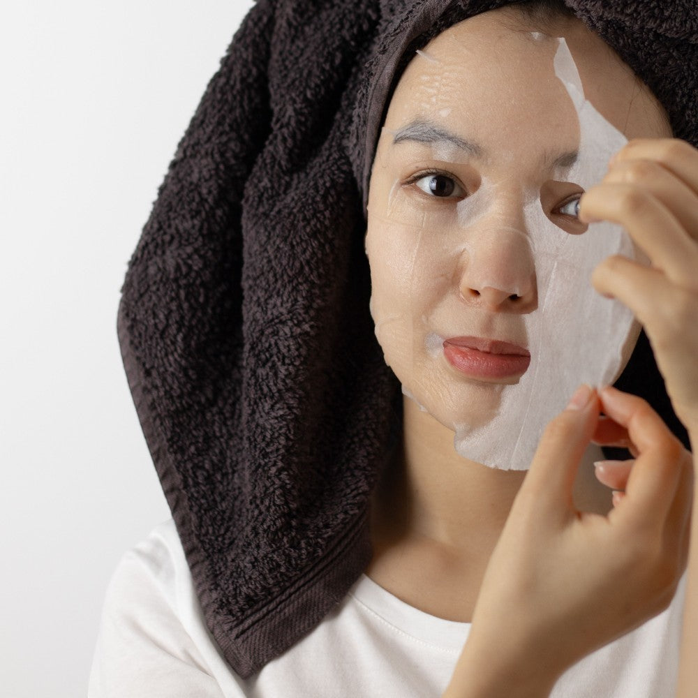 Skin TOGO Seoul Girl's Beauty Secret Vitalizing sheet mask being applied by a woman with a dark towel on her head.